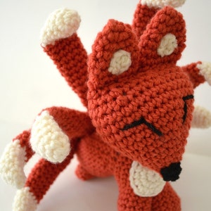 May include: A crocheted red fox with white accents on its ears, paws, and tail. The fox has a black nose and embroidered eyes.