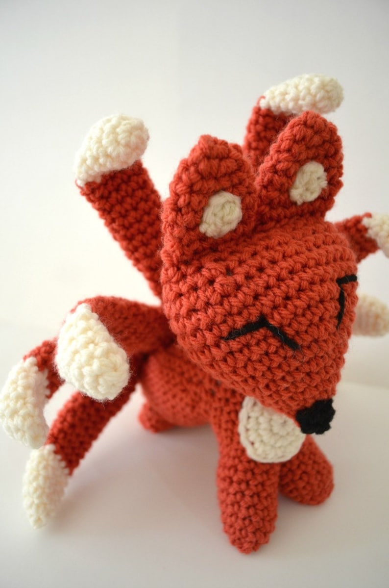 May include: A crocheted red fox with white accents on its ears, paws, and tail. The fox has a black nose and embroidered eyes.