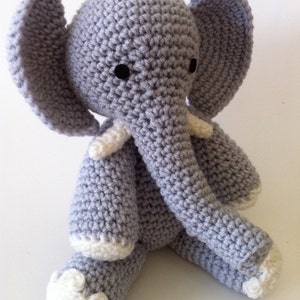 May include: A gray crocheted elephant toy with white accents on the ears, trunk, and feet. The elephant has black eyes and a stitched smile.