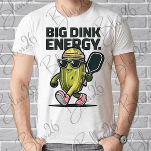 May include: White t-shirt featuring a cartoon pickle wearing sunglasses and holding a paddle. The text "BIG DINK ENERGY." is printed on the shirt.