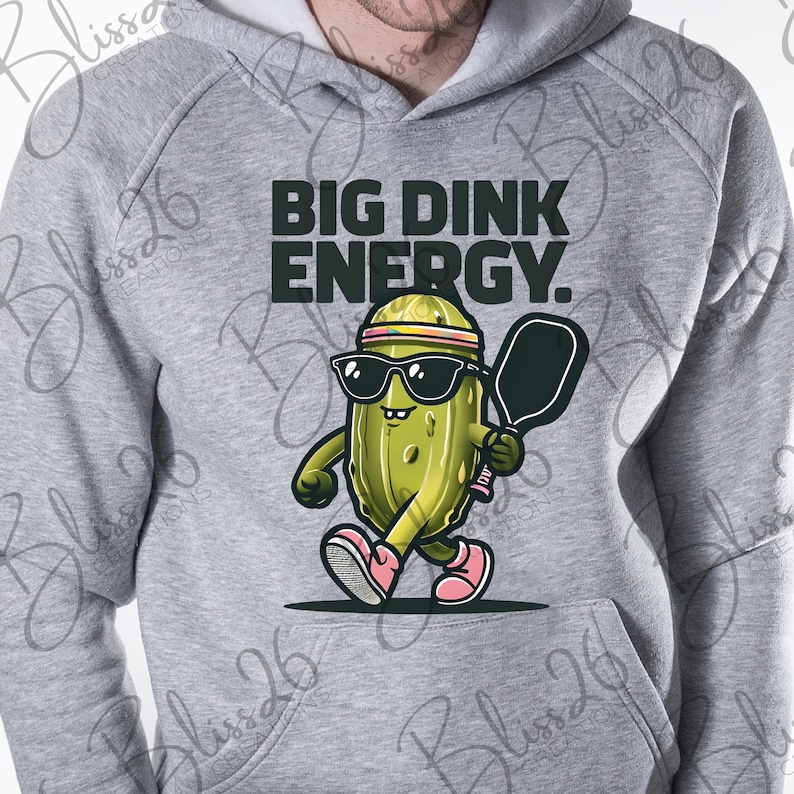 May include: A grey hoodie featuring a pickle character wearing sunglasses and a headband, holding a pickleball paddle. The text "BIG DINK ENERGY." is printed on the hoodie.