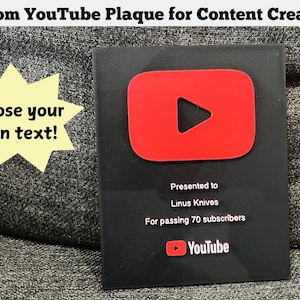 May include: A black plaque with a red YouTube play button logo. The plaque reads "Custom YouTube Plaque for Content Creators!" and "Choose your own text!". It is presented to Linus Knives for passing 70 subscribers.