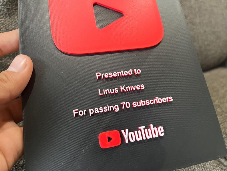 May include: A black and red YouTube Play Button award. The award is presented to Linus Knives for passing 70 subscribers. The YouTube logo is visible at the bottom of the award.