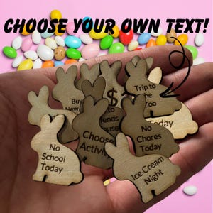 May include: A hand holding a variety of wooden bunny shapes with different phrases written on them, such as "No School Today", "Trip to the Zoo", and "Ice Cream Night".