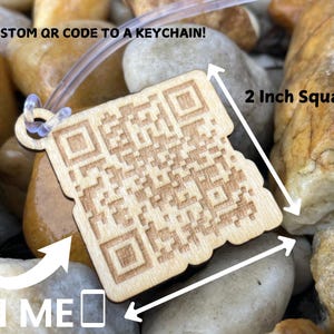 May include: A wooden keychain with a laser-engraved QR code. The keychain is 5 cm square and has a clear plastic loop for attaching to keys. The text "SCAN ME" is printed on the keychain.