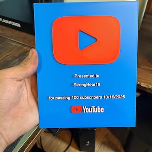 May include: A blue plaque with a red YouTube play button logo. The plaque reads "Presented to StrongBear19 for passing 100 subscribers 10/16/2025" and includes the YouTube logo.