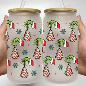 May include: Two frosted glass tumblers with bamboo lids and straws. The tumblers feature a repeating pattern of the Grinch's hand holding a Christmas tree with red and white stripes, snowflakes, and red stars.