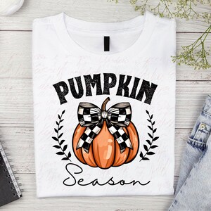 May include: White t-shirt with a black and white checkered bow on top of an orange pumpkin. The text "Pumpkin Season" is written in black below the pumpkin.