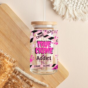 Puede incluir: Un vaso de vidrio transparente con tapa de bamb&uacute; y un dise&ntilde;o rosa y negro de "True Crime Addict". El vaso tiene un dise&ntilde;o de cinta de escena del crimen en blanco y negro alrededor de la parte superior e inferior.