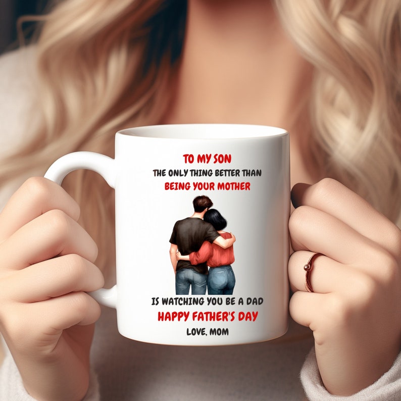 Peut inclure: Mug en c&eacute;ramique blanche avec un message qui dit "&Agrave; mon fils, la seule chose qui soit mieux que d'&ecirc;tre ta m&egrave;re, c'est de te voir devenir p&egrave;re. Joyeuse f&ecirc;te des p&egrave;res. Avec amour, Maman". La tasse pr&eacute;sente une illustration de dessin anim&eacute; d'un couple qui s'embrasse.
