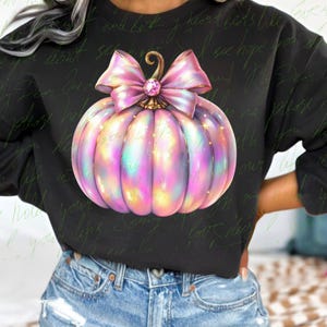 May include: A black sweatshirt with a pink and iridescent glitter pumpkin with a pink bow. The pumpkin has a gold stem and a sparkly rhinestone in the center of the bow.
