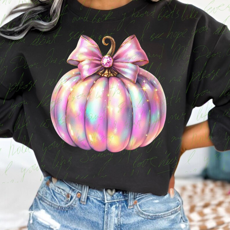 May include: A black sweatshirt with a pink and iridescent glitter pumpkin with a pink bow. The pumpkin has a gold stem and a sparkly rhinestone in the center of the bow.
