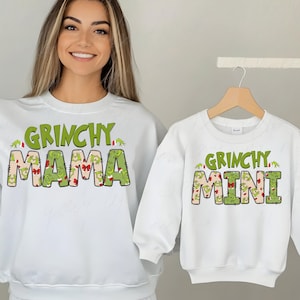 May include: White sweatshirts with green and red Grinch-themed text. The larger sweatshirt says "Grinchy Mama" and the smaller sweatshirt says "Grinchy Mini".
