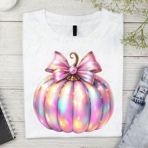 May include: A white t-shirt with a pink and iridescent pumpkin with a pink bow and a rhinestone in the center.