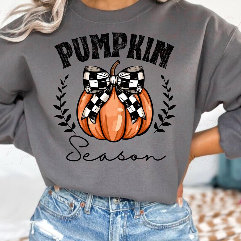 May include: A gray sweatshirt with the text "Pumpkin Season" in black. A black and white checkered bow is tied around an orange pumpkin.