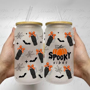 Op de afbeelding: Twee frosted glazen bekers met deksels en rietjes. De bekers hebben een Halloween-thema met een pompoen, vleermuizen en spinnenwebben. Een beker heeft de tekst "SPOOKY vibes".