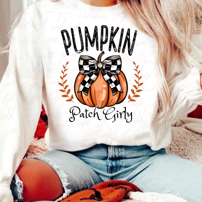 K&ouml;nnte beinhalten: Wei&szlig;er Pullover mit einem schwarz-wei&szlig; karierten K&uuml;rbis mit Schleife und dem aufgedruckten Text "Pumpkin Patch Girly".