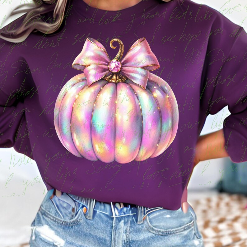 May include: A purple sweatshirt with a sparkly iridescent pumpkin with a pink bow. The pumpkin has a gold stem and a large pink rhinestone in the center of the bow.