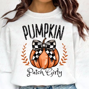 K&ouml;nnte beinhalten: Wei&szlig;es Sweatshirt mit einem schwarzen und orangefarbenen K&uuml;rbis-Motiv. Der K&uuml;rbis hat eine schwarz-wei&szlig;e karierte Schleife und der Text "Pumpkin Patch Girly" befindet sich unter dem K&uuml;rbis.