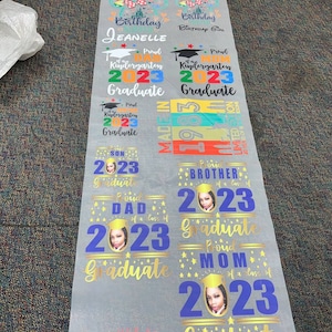 May include: A roll of printed heat transfer vinyl featuring various designs. Designs include "Birthday" with Minnie Mouse, "Proud Kindergarten Graduate 2023", and "Proud Dad of a class of 2023 Graduate". The designs are in various colors.