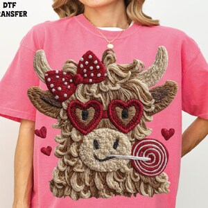 Pode incluir: Camiseta rosa com um design bordado de uma vaca das Terras Altas com &oacute;culos de sol em forma de cora&ccedil;&atilde;o, um la&ccedil;o e um pirulito. A vaca tem um rosto sorridente e &eacute; cercada por pequenos cora&ccedil;&otilde;es. O texto "DTF TRANSFER" est&aacute; no canto superior esquerdo.