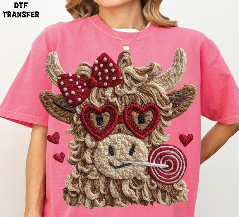 Pode incluir: Camiseta rosa com um design bordado de uma vaca das Terras Altas com &oacute;culos de sol em forma de cora&ccedil;&atilde;o, um la&ccedil;o e um pirulito. A vaca tem um rosto sorridente e &eacute; cercada por pequenos cora&ccedil;&otilde;es. O texto "DTF TRANSFER" est&aacute; no canto superior esquerdo.