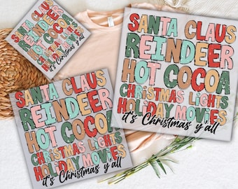 May include: DTF transfers with a Christmas theme. The transfers feature the words "Santa Claus, Reindeer, Hot Cocoa, Christmas Lights, Holiday Movies, it's Christmas y'all" in a colorful, distressed font. A peach-colored t-shirt is also visible.