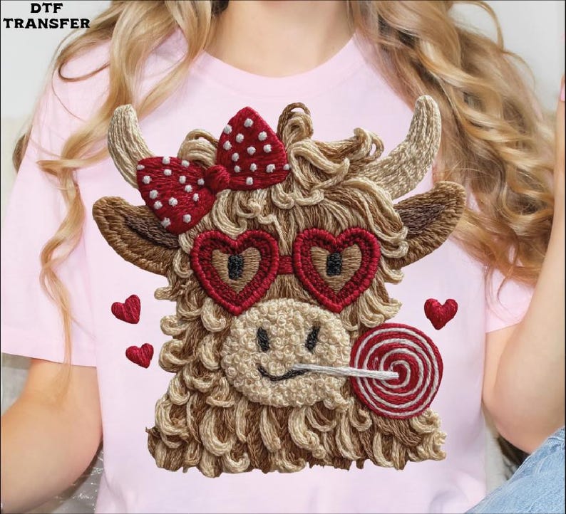 Pode incluir: Camiseta rosa com um design bordado de vaca das Terras Altas. A vaca tem &oacute;culos de sol em forma de cora&ccedil;&atilde;o, um la&ccedil;o vermelho com bolinhas brancas e um pirulito. Pequenos cora&ccedil;&otilde;es vermelhos est&atilde;o espalhados ao redor da vaca.