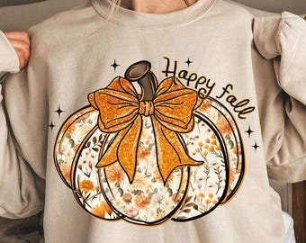 Pode incluir: Camisola bege com um design de abóbora com um laço laranja brilhante e um padrão floral. As palavras "Happy fall" estão escritas em preto. Estrelas pretas completam o tema outonal.