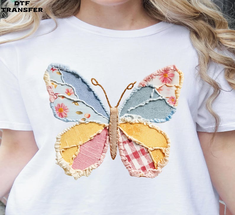 May include: White t-shirt featuring a colorful butterfly design. The butterfly has patchwork wings in shades of blue, yellow, pink, and red, with floral and gingham patterns. The text "DTF TRANSFER" is in the upper left corner.