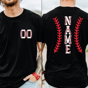 May include: Black t-shirt with baseball-themed graphics. The front features the number "00" in a baseball design. The back displays the word "NAME" in a baseball font, flanked by red baseball stitching.