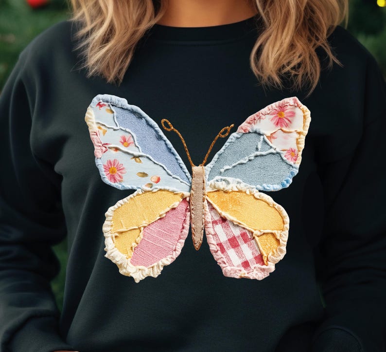 May include: Black sweatshirt featuring a colorful butterfly applique. The butterfly design incorporates floral, gingham, and denim-like fabrics in shades of blue, pink, yellow, and red. The butterfly's body and antennae are a tan color.