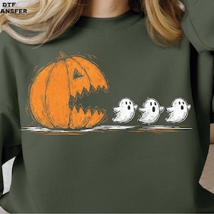 May include: Dark green sweatshirt featuring a Halloween-themed graphic. An orange jack-o'-lantern with a jagged mouth is positioned to the left, with three white cartoon ghosts to the right. The text "DTF TRANSFER" is in the upper left corner.