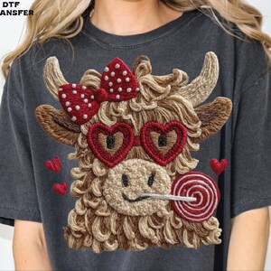 Pode incluir: Camiseta cinza escuro com um design de vaca bordada. A vaca tem &oacute;culos de sol em forma de cora&ccedil;&atilde;o, um la&ccedil;o vermelho com bolinhas brancas e um pirulito. Pequenos cora&ccedil;&otilde;es vermelhos est&atilde;o espalhados ao redor da vaca.