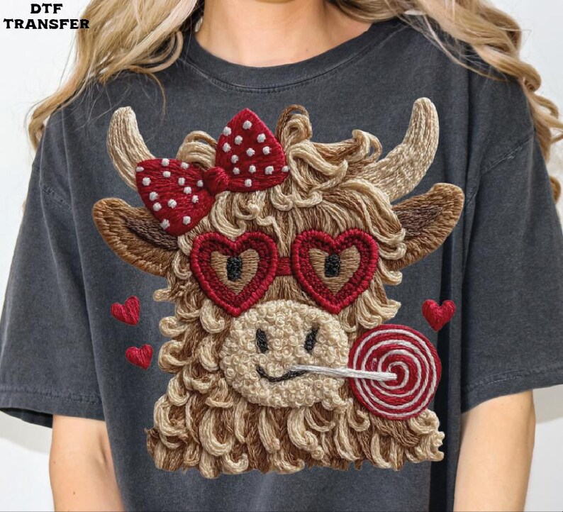 Pode incluir: Camiseta cinza escuro com um design de vaca bordada. A vaca tem &oacute;culos de sol em forma de cora&ccedil;&atilde;o, um la&ccedil;o vermelho com bolinhas brancas e um pirulito. Pequenos cora&ccedil;&otilde;es vermelhos est&atilde;o espalhados ao redor da vaca.
