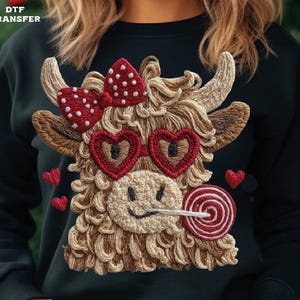 Pode incluir: Camisola preta com um design bordado de uma vaca das Terras Altas. A vaca usa &oacute;culos em forma de cora&ccedil;&atilde;o, um la&ccedil;o de bolinhas e um pirulito. Pequenos cora&ccedil;&otilde;es vermelhos est&atilde;o espalhados ao redor do design. O texto "DTF TRANSFER" est&aacute; no canto superior esquerdo.