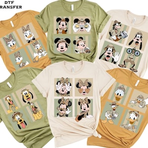 May include: A collection of t-shirts in various colors, each featuring a unique design with cartoon characters. The designs include Mickey Mouse, Minnie Mouse, Donald Duck, and Goofy, with safari-themed and leopard print elements.