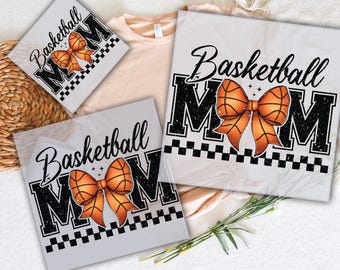 Puede incluir: Tres diseños de transferencia de calor para camisetas con el texto "Basketball Mom" con un diseño de baloncesto y lazo. Los diseños están en hojas transparentes listas para ser presionadas sobre la tela.