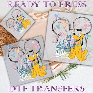 May include: A digital design featuring a cartoon image of Pluto, the Disney dog, standing in front of Cinderella's Castle. The design is surrounded by a Mickey Mouse ear outline and colorful balloons. The text "READY TO PRESS" and "DTG TRANSFERS" are also included in the design.