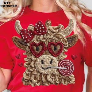 Pode incluir: Camiseta vermelha com um design bordado de vaca Highland. A vaca usa &oacute;culos de sol em forma de cora&ccedil;&atilde;o, um la&ccedil;o e um pirulito. O design inclui o texto "DTF TRANSFER" no canto superior esquerdo.