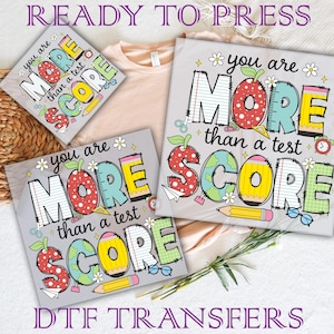 May include: Three iron-on transfers with a colourful design featuring the text "You are more than a test score". The design is made to look like a patchwork of different fabrics and includes a pencil, a globe, and a pair of glasses.