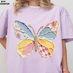 May include: A light purple t-shirt featuring a large, colorful butterfly applique. The butterfly has wings made of patchwork fabric in shades of blue, yellow, pink, and red, with floral and gingham patterns. The text "DTF TRANSFER" is in the upper left corner.