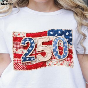May include: White t-shirt featuring a patriotic design with the number "250" in a patchwork style. The design incorporates red, white, and blue elements, including stars and stripes, creating a vintage aesthetic. The text "DTF TRANSFER" is visible in the top left corner.