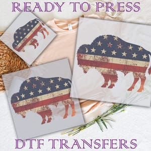 May include: DTF transfers featuring a distressed American flag design in the shape of a bison. The transfers have a vintage look with red and white stripes and blue stars. The words "READY TO PRESS" and "DTF TRANSFERS" are visible.
