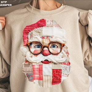 May include: Beige sweatshirt featuring a Santa Claus face design. The Santa face is made of patchwork fabric with a red hat, glasses, and a white beard. The text "DTF TRANSFER" is in the upper left corner.