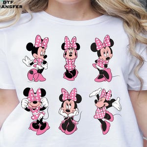 Peut inclure: T-shirt blanc avec plusieurs images de Minnie Mouse dans différentes poses. Chaque personnage de Minnie Mouse porte une robe rose à pois, un nœud assorti et des chaussures. Le texte "DTF TRANSFER" est imprimé en haut à gauche.