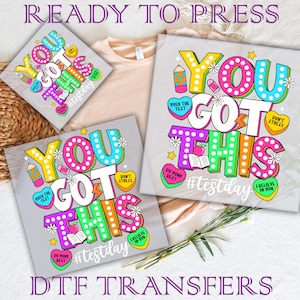 May include: Three iron-on transfers with the text "You Got This" in colorful, outlined letters with a lightbulb design. The transfers also include the text "#testday" and other motivational phrases.