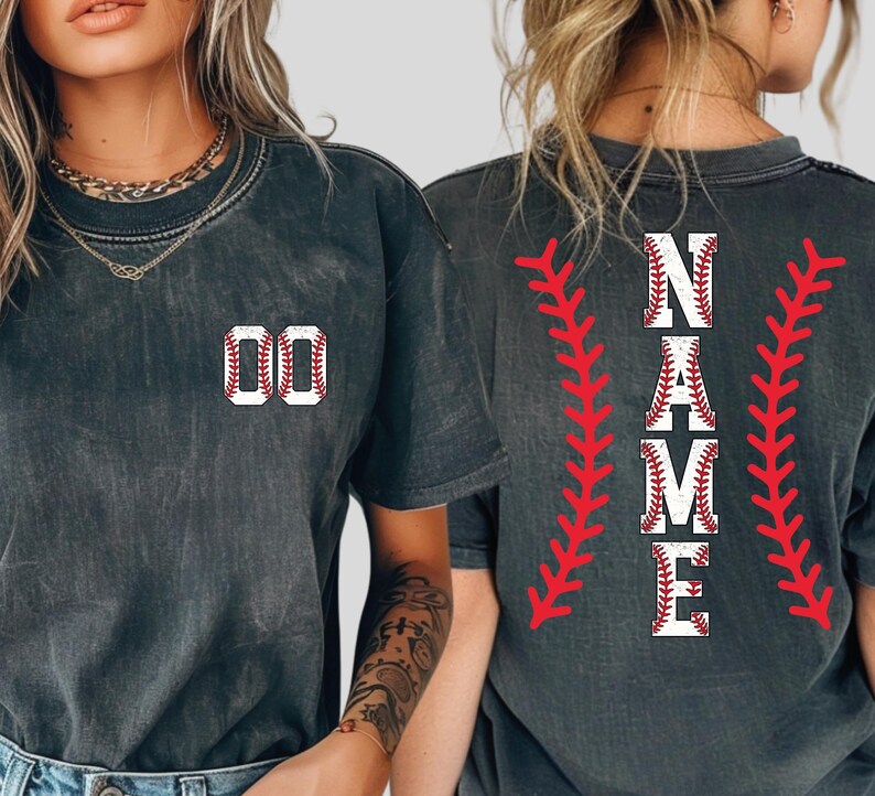 May include: Dark gray t-shirts with baseball-themed designs. One shirt features the number "00" in a baseball stitch design. The other shirt displays the word "NAME" in a baseball stitch design, with red stitching accents.