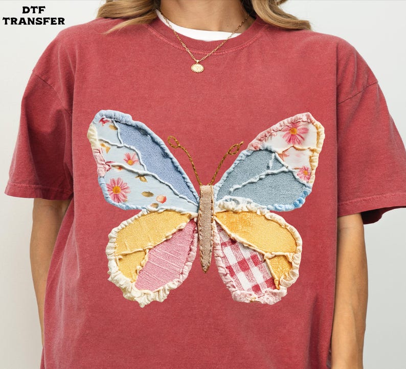 May include: A red-orange t-shirt featuring a large, colorful butterfly applique. The butterfly wings are patchwork, with floral, denim, and gingham patterns. The shirt has short sleeves and a crew neck.