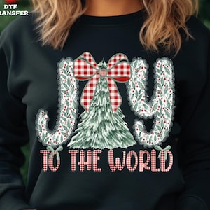 May include: Black sweatshirt with a Christmas-themed graphic. The design features the words "JOY TO THE WORLD" in a festive font, a plaid bow, and a Christmas tree. The letters are decorated with holly and berries.